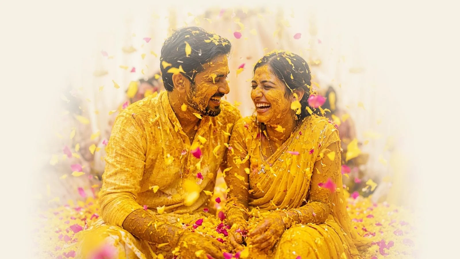 A laughing couple at their haldi, covered in turmeric, as marigold and rose petals rain down